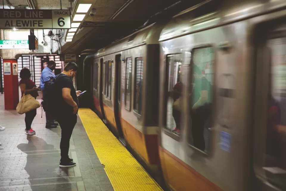 Passengers on Boston subway platform with blurred speeding train passing by